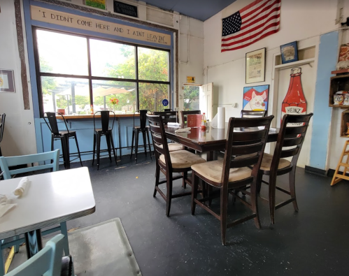A cozy diner interior with empty tables, a large window, and American decor, including an American flag and Heinz ketchup bottle.