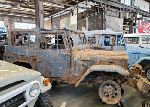 A rusted, vintage off-road vehicle displayed in a museum, surrounded by other classic cars.