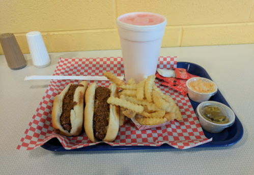 A tray with two hot dogs, crinkle-cut fries, dipping sauces, and a large drink on a checkered paper.