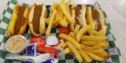 A tray with three hot dogs topped with chili, crinkle-cut fries, coleslaw, and condiments.