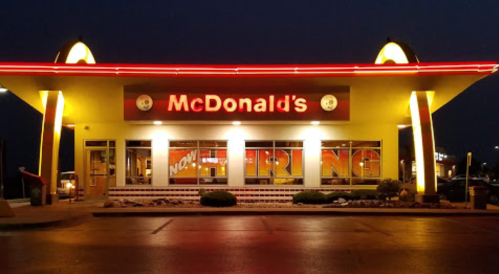 A brightly lit McDonald's restaurant at night, featuring a "Now Hiring" sign and a colorful exterior.
