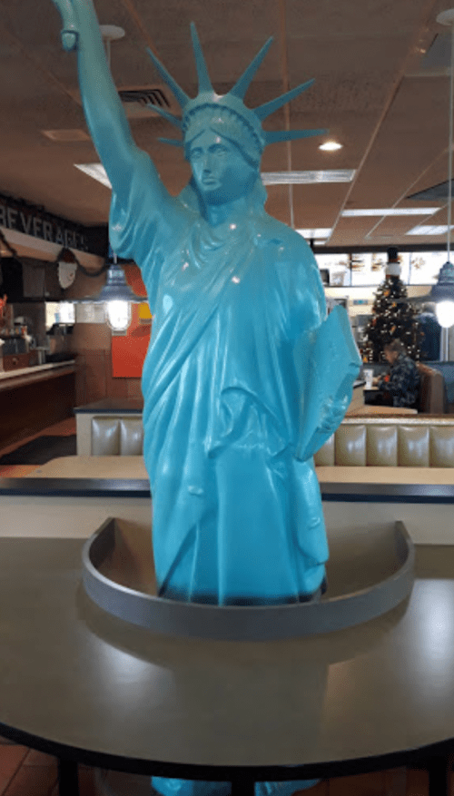 A blue statue of Liberty stands in a diner, surrounded by a circular table and casual dining decor.