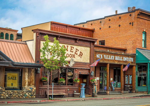 Historic buildings with wooden facades and storefronts, featuring flags and greenery in a quaint town setting.