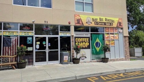 Exterior of Busy Bee Roasters Coffee Shop, featuring a Brazilian flag and an American flag, with a convenience store sign.