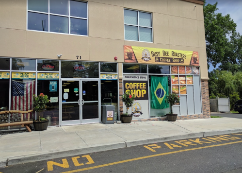 Exterior of Busy Bee Roasters coffee shop, featuring a Brazilian flag, signage, and a "No Parking" area.