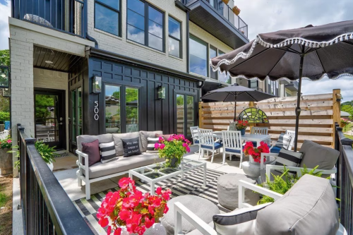 A stylish outdoor patio with seating, umbrellas, and vibrant flowers, set against a modern building.