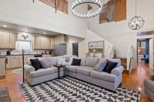 Cozy living room with a large sectional sofa, modern chandelier, and open kitchen in a rustic-style home.