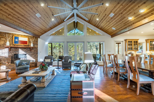Spacious living room with wooden ceiling, large windows, and cozy furniture, featuring a dining area and rustic decor.