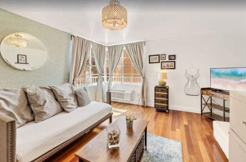 Cozy living room with a sofa, wooden coffee table, decorative mirror, and stylish curtains, featuring warm wooden floors.