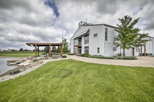 A modern building beside a landscaped area with a pond, stone pathway, and a shaded seating area under a pergola.