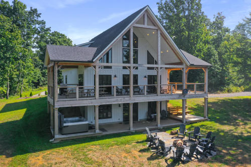 A modern two-story house with a large deck, surrounded by trees and a fire pit area in the yard.