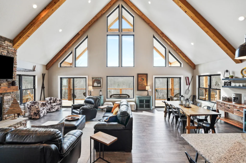 Spacious living area with high ceilings, large windows, and a mix of modern and rustic furniture.