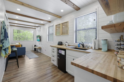 Bright, modern kitchen with wooden beams, white walls, and a cozy seating area, featuring a sink and appliances.