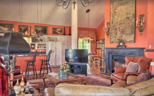Cozy living room with warm colors, a fireplace, and a kitchen area, featuring vintage decor and comfortable seating.