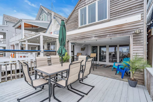 Outdoor patio with a dining table and chairs, overlooking a waterfront view, surrounded by beach-style houses.