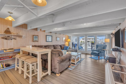 Cozy living room with wooden beams, a large sofa, dining table, and access to a deck with water views.