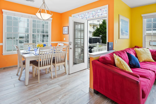 Bright dining area with a table set for six, a red sofa, and large windows opening to an outdoor view.