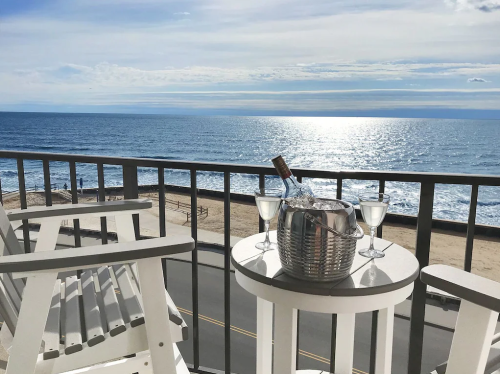 A balcony view overlooking the ocean, featuring a bottle of champagne and two glasses on a table.