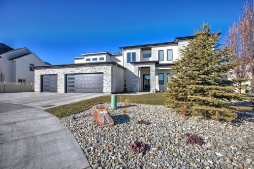 Modern two-story house with stone accents, large windows, and a landscaped front yard featuring rocks and shrubs.