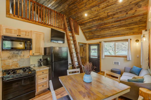 Cozy cabin interior featuring a kitchen, dining area, and lofted sleeping space with wooden accents and natural light.