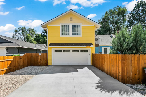 A bright yellow house with a white garage, surrounded by a wooden fence and a clear blue sky.