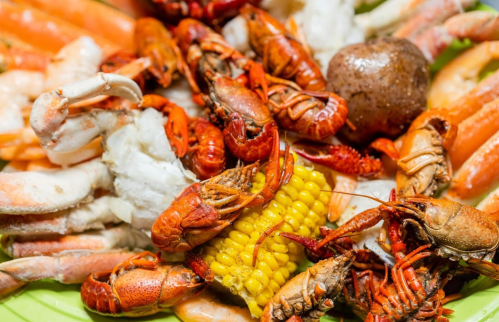 A colorful seafood platter featuring crawfish, crab legs, shrimp, and corn on a green plate.