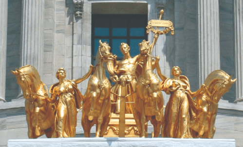 Golden statue of a charioteer with horses, flanked by two figures, atop a building with classical architecture.