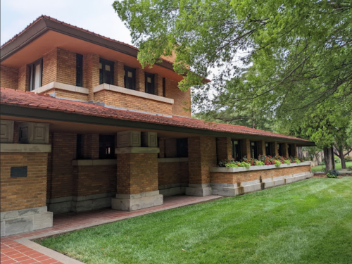 A brick building with a red tile roof, surrounded by green grass and trees, showcasing a classic architectural style.