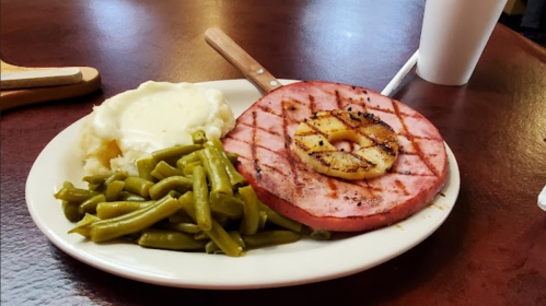 A plate with grilled ham steak topped with pineapple, green beans, and mashed potatoes.