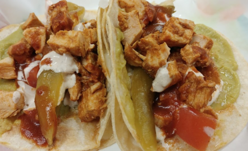Two tacos filled with shredded chicken, green peppers, diced tomatoes, and drizzled with sauce.