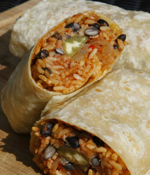 A close-up of a cut burrito filled with rice, beans, and vegetables, resting on a wooden surface.