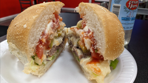 A close-up of a sandwich with layers of meat, cheese, lettuce, tomatoes, and condiments, served on a white plate.