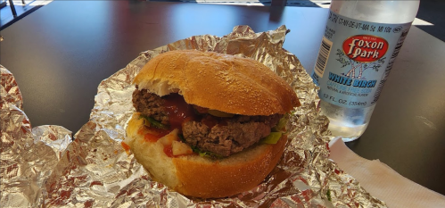 A hamburger with lettuce, ketchup, and a soft bun, next to a bottle of soda on a table.