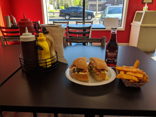 A table with two sandwiches, sweet potato fries, and condiments in a restaurant with a red wall and a window view.
