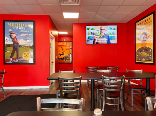Interior of a restaurant with red walls, tables, and a TV displaying a cooking show, featuring framed posters.