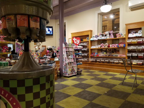 A colorful store interior featuring a candy machine, plush toys, and shelves filled with various merchandise.