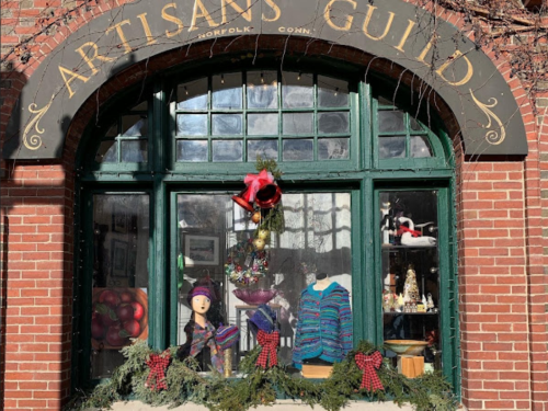 A festive storefront display featuring handmade crafts, colorful garments, and holiday decorations.