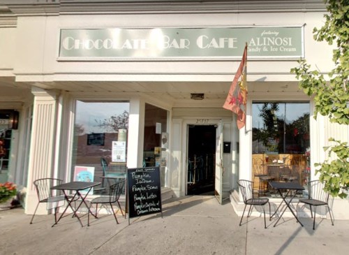 Exterior of Chocolate Bar Café featuring outdoor seating and a sign with menu items.