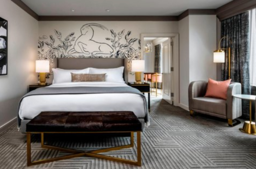 A stylish hotel room featuring a king bed, modern decor, a seating area, and artistic wall design.