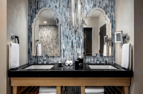 Modern bathroom with dual sinks, stylish mirrors, and a textured blue wall. White towels neatly arranged.