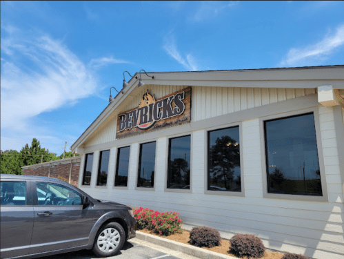 Exterior of a restaurant named "Bevericks," featuring large windows and a parked car in front. Clear blue sky above.