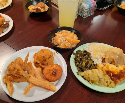 A table with two plates of Southern food, including fried chicken, cornbread, collard greens, and peach cobbler.