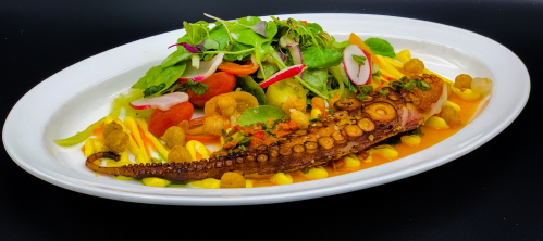 A beautifully plated dish featuring grilled octopus, vibrant salad, and colorful garnishes on a white platter.