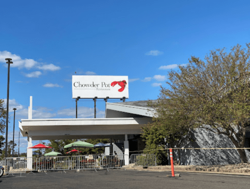 Exterior of Chowder Pot Restaurant with a sign, outdoor seating, and a clear blue sky.