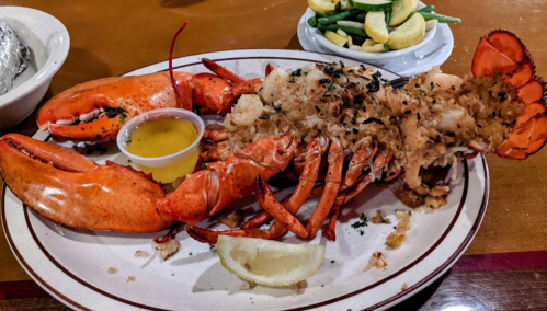A plate featuring a whole lobster with a side of melted butter and lemon, accompanied by a vegetable medley.