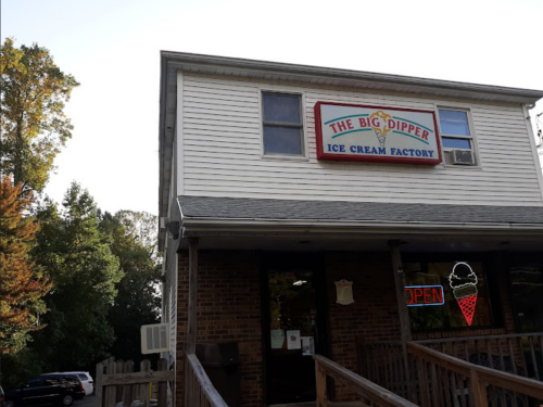 Exterior of The Big Dipper Ice Cream Factory, featuring a sign and an open neon light, surrounded by trees.