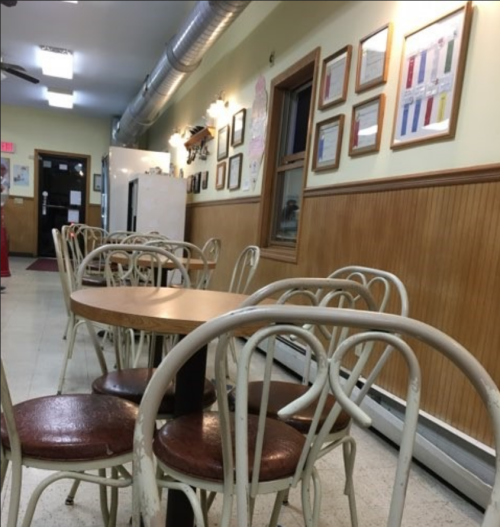 A cozy café interior with wooden tables and chairs, featuring a warm color scheme and framed pictures on the walls.