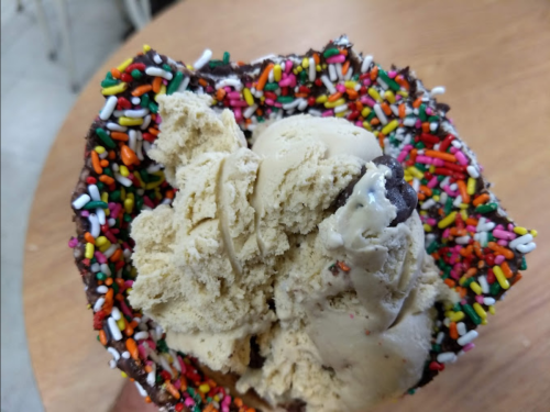 A heart-shaped ice cream cone filled with two scoops of ice cream and topped with colorful sprinkles.