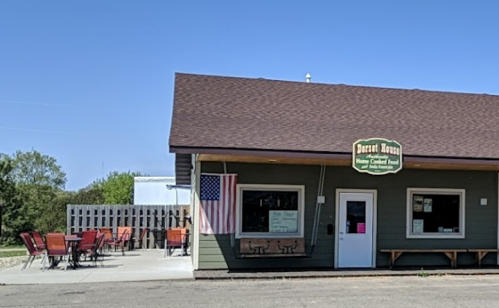 A small restaurant with a sign reading "Desert House," featuring outdoor seating and an American flag.