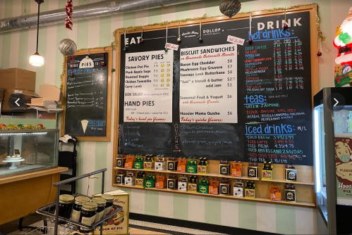 Menu board featuring savory pies, biscuit sandwiches, and drinks in a cozy café setting with green striped walls.